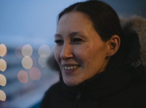 A woman in Nuuk, Greenland, smiles warmly in a winter coat at twilight. A woman in Nuuk, Greenland, smiles warmly in a winter coat at twilight.