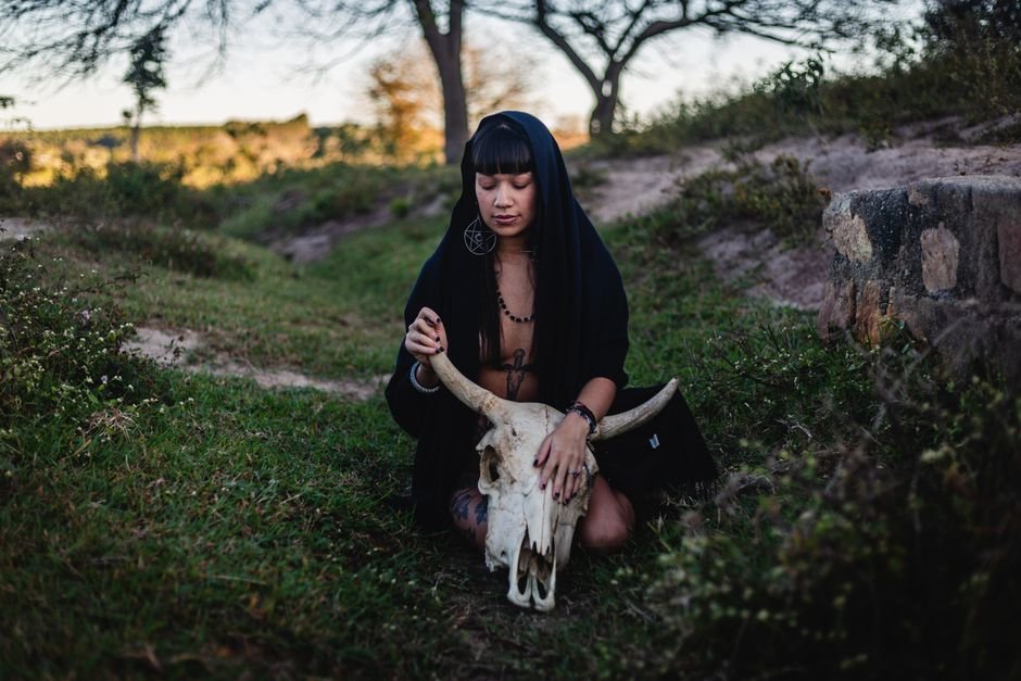 Cypriot Horror Film ‘Motherwitch’ Secures North American Distribution Ahead of Sitges Premiere A woman in a black hooded cloak holding a large animal skull in a grassy outdoor setting.