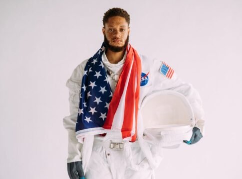 Astronaut wearing a suit holding a helmet and draped in an American flag. Astronaut wearing a suit holding a helmet and draped in an American flag.
