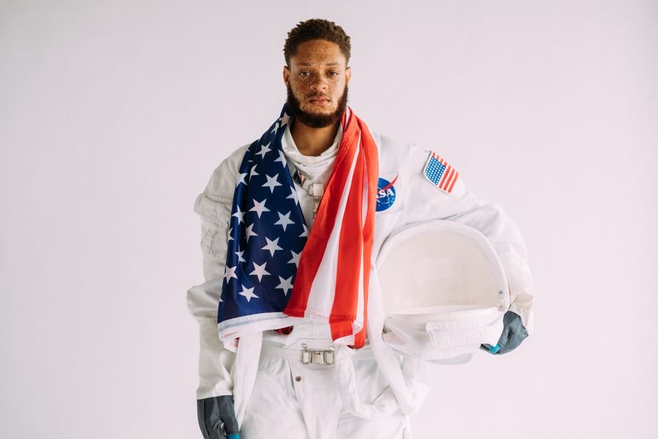 Stars Jalen Brunson and Joe Burrow Endorse BODYARMOR, Drinks Now on Sale Astronaut wearing a suit holding a helmet and draped in an American flag.