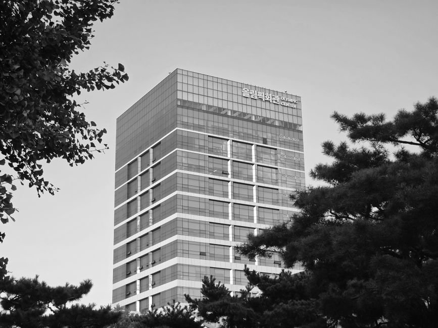 CJ ENM and MBC Group Forge Strategic Alliance to Amplify Korean Entertainment in MENA Region Black and white photo of Olympic Center building in Seoul framed by trees.