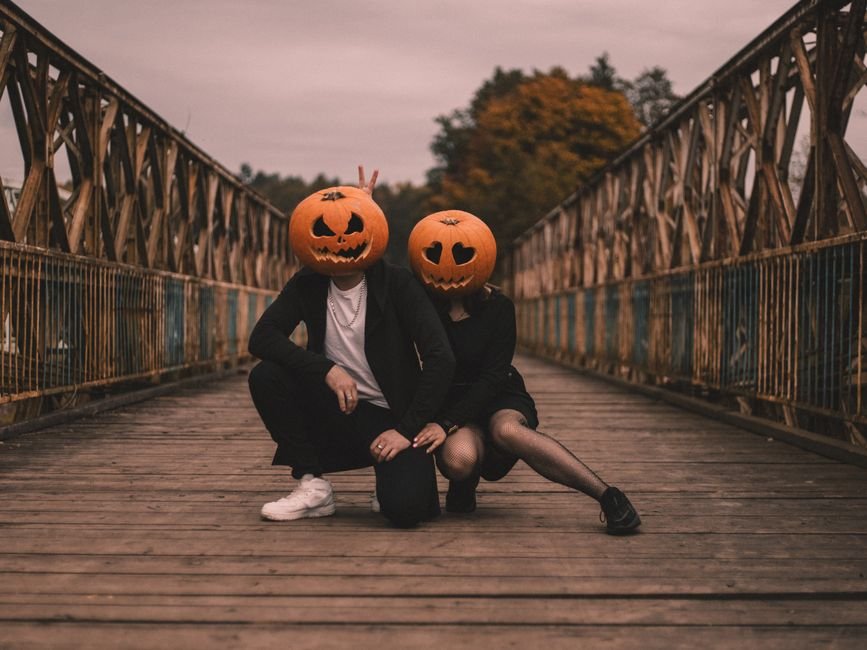 Celebrity Couples Dominate Halloween with Show-Stopping Duo Costumes Couple in Halloween costumes with pumpkin heads on an old wooden bridge, adding a spooky charm to the scene.