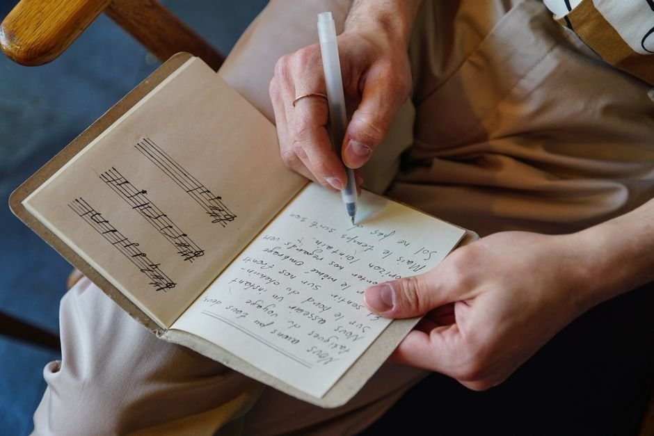 ‘The Notebook’ Musical Secures West End Debut at Renamed Judi Dench Theatre Male songwriter writes lyrics and music notes in a notebook, capturing the creative process.
