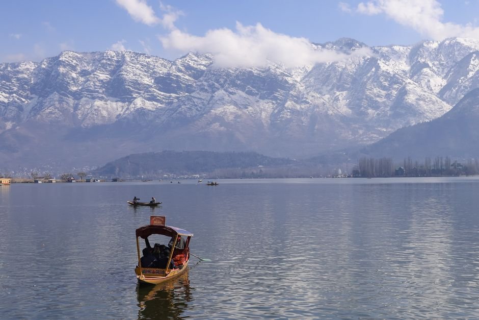 Jammu and Kashmir Poised for Adventure Tourism Boom, Says Shahid Muzaffar Peaceful view of Dal Lake in Srinagar surrounded by snowcapped Himalayas, featuring traditional boats.