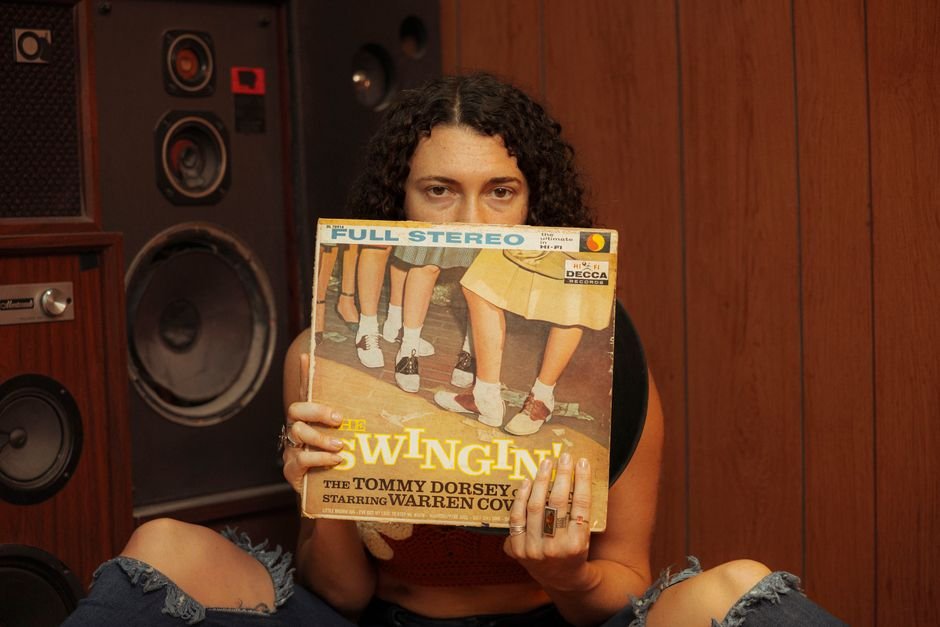 Diane Warren Tapped to Pen Original Song for ‘Armani: The King of Fashion’ Biopic Person holding a vintage vinyl record in front of retro speakers, evoking a classic music ambiance.