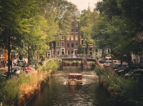 Picturesque view of a boat on an Amsterdam canal surrounded by lush greenery and classic architecture. Picturesque view of a boat on an Amsterdam canal surrounded by lush greenery and classic architecture.