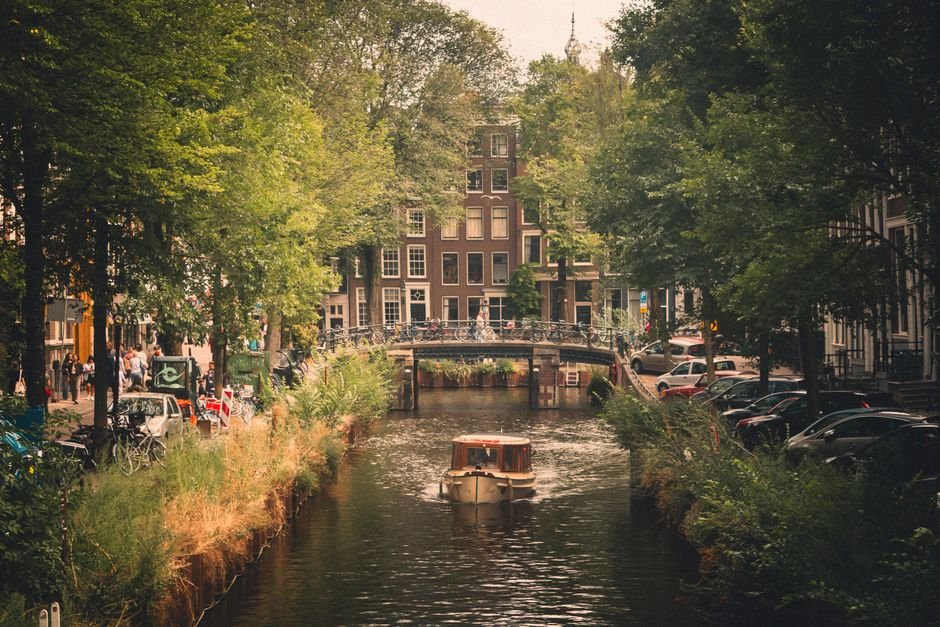 Canal+ Threatens $1.1 Billion French Cinema Investment Over Tax Hike Picturesque view of a boat on an Amsterdam canal surrounded by lush greenery and classic architecture.