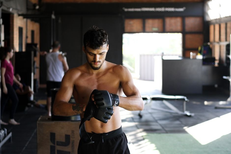 How to Stream UFC 333: Volkanovski vs. Evloev Online Shirtless man preparing for an intense workout session in a gym, wearing boxing gloves.