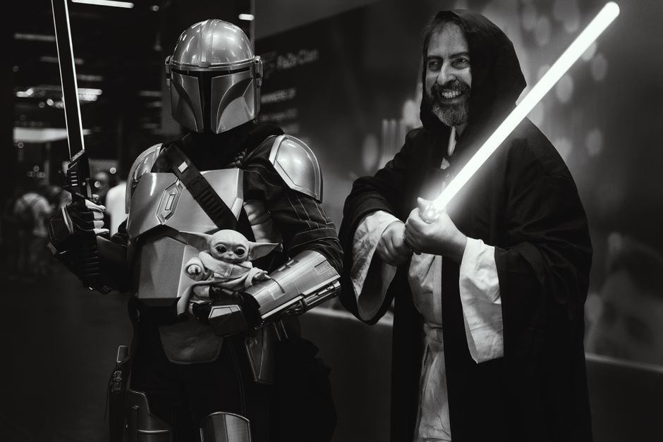 Hal Hickel on ‘The Mandalorian and Grogu’ VFX: Embracing Phil Tippett’s Legacy and Favreau’s Vision Star Wars fans in Mandalorian and Jedi costumes wielding swords at an event.